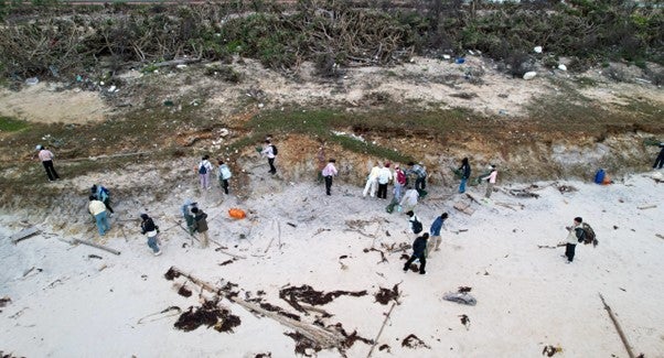 Group of students picking up trash off of beach as seen from above