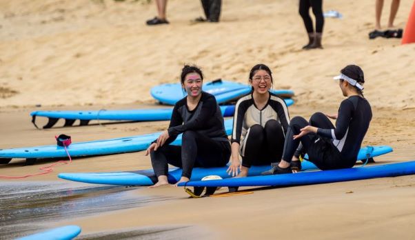 HAIC students sitting on surfboard on beach chatting