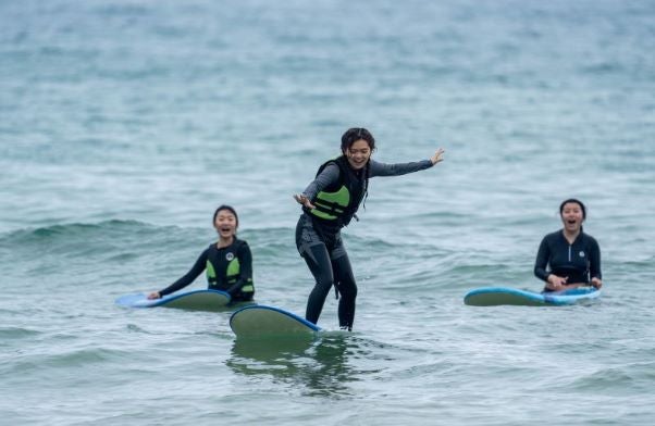 HAIC student surfing with 2 students sitting on surfboards behind her