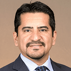 Alberto Olivas headshot - fair-skinned man, smiling, black hair and mustache, gray blazer, white collared shirt, blue tie
