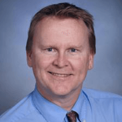 David Swindell headshot - fair-skinned man, smiling, brown hair, blue collared shirt, maroon tie