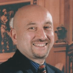 Flavio Marsiglia headshot - fair-skinned man, smiling, bald, black blazer, blue-striped collared shirt, red-and-navy-striped tie