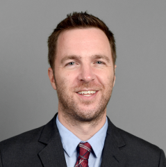 Kevin Wright headshot - fair-skinned man, smiling, brown hair, black blazer, light blue collared shirt, red tie 