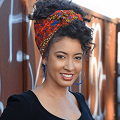 Chandra Crudup headshot - medium-skinned woman, smiling, black hair, orange and blue hair scarf, black shirt, blue earrings