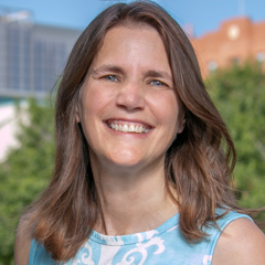 Elizabeth Lightfoot headshot - fair-skinned woman, smiling, brown hair, blue and white shirt